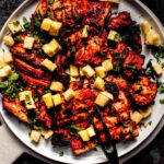 Cook al pastor chicken thighs on plate with chopped pineapple and cilantro.