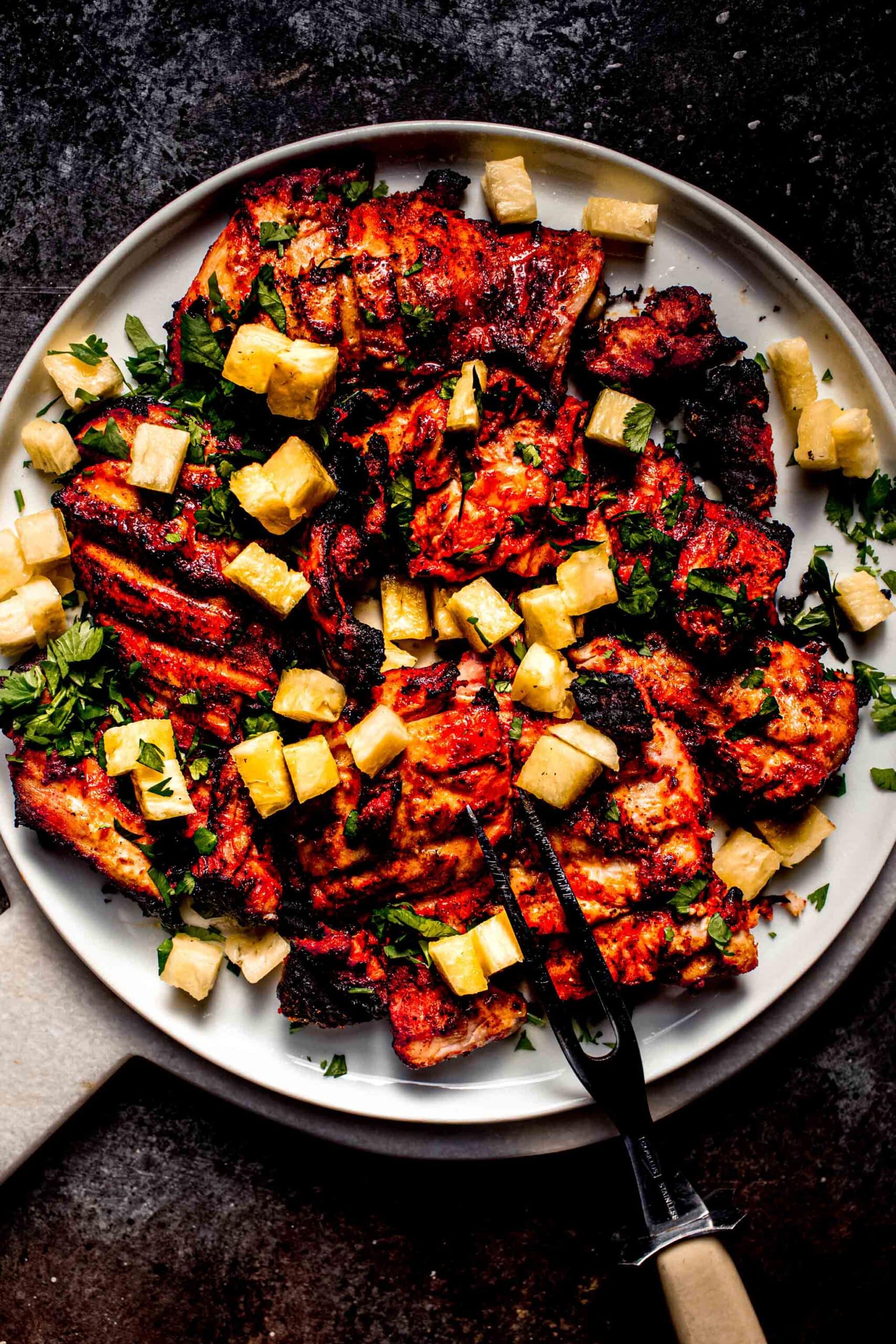 Cook al pastor chicken thighs on plate with chopped pineapple and cilantro.