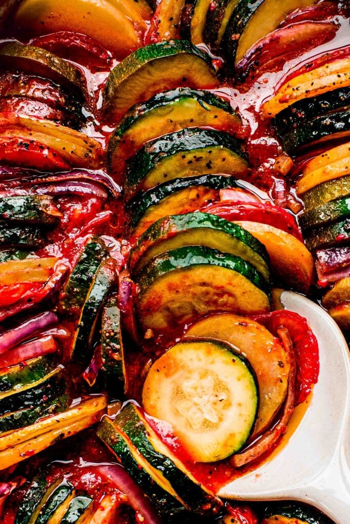 Close up of Briam roasted vegetables in baking dish with serving spoon.