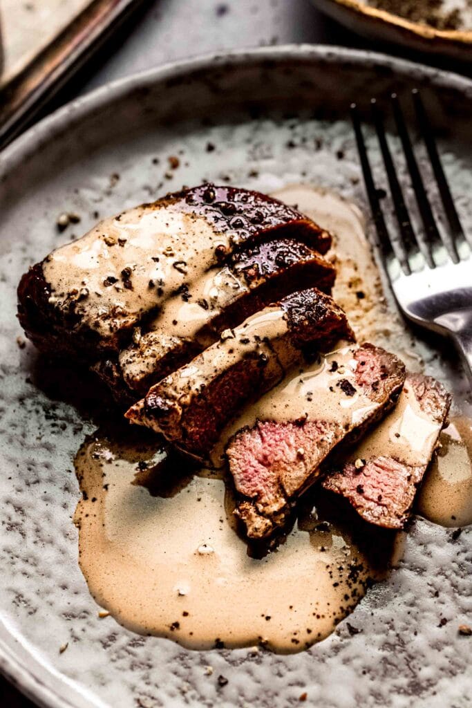 Side view of Sliced steak on plate drizzled with peppercorn sauce.