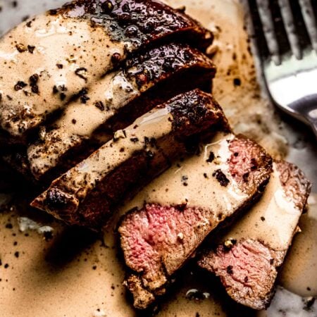 Sliced steak on plate drizzled with peppercorn sauce.