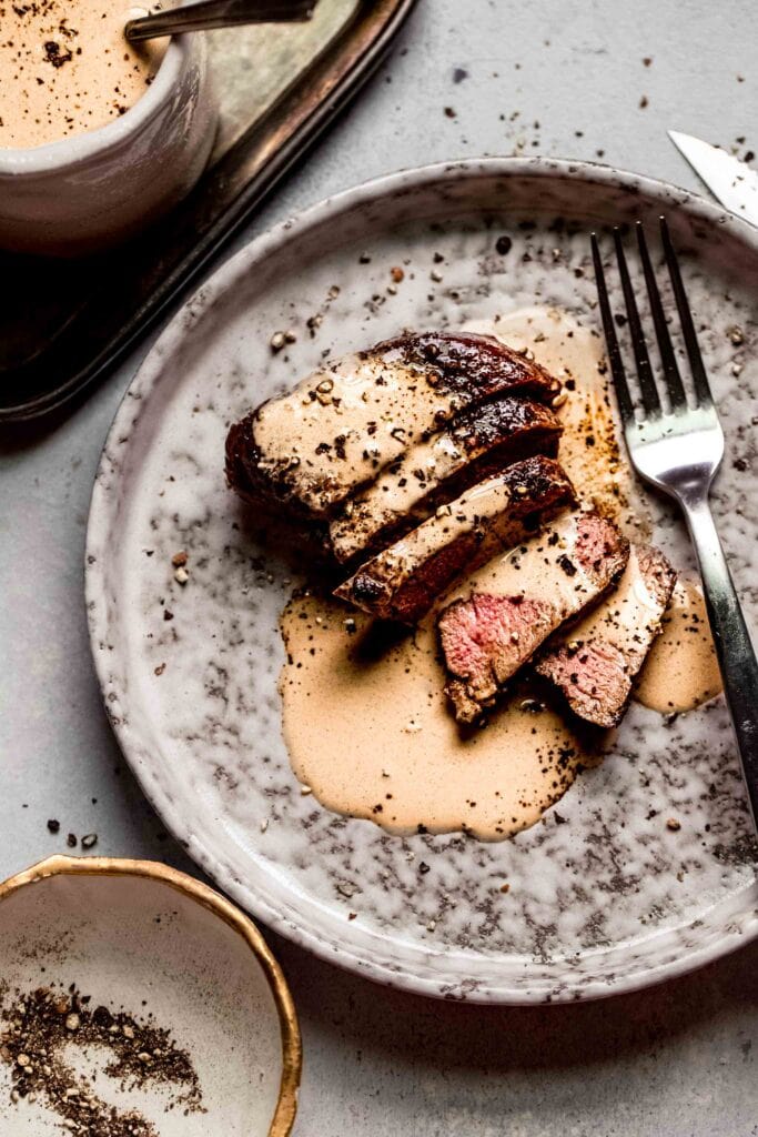 Sliced steak on plate drizzled with peppercorn sauce.