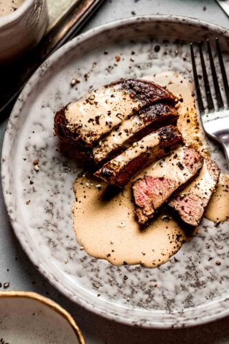Sliced steak on plate drizzled with peppercorn sauce.