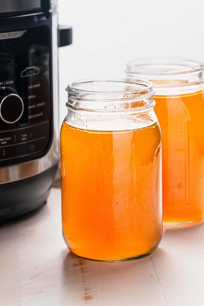 Side view of two jars of bone broth next to instant pot.