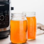 Side view of two jars of bone broth next to instant pot.