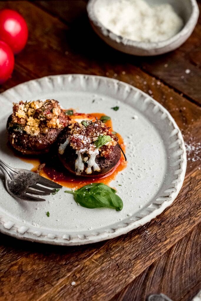 Two Italian stuffed mushrooms on plate with basil leaf.