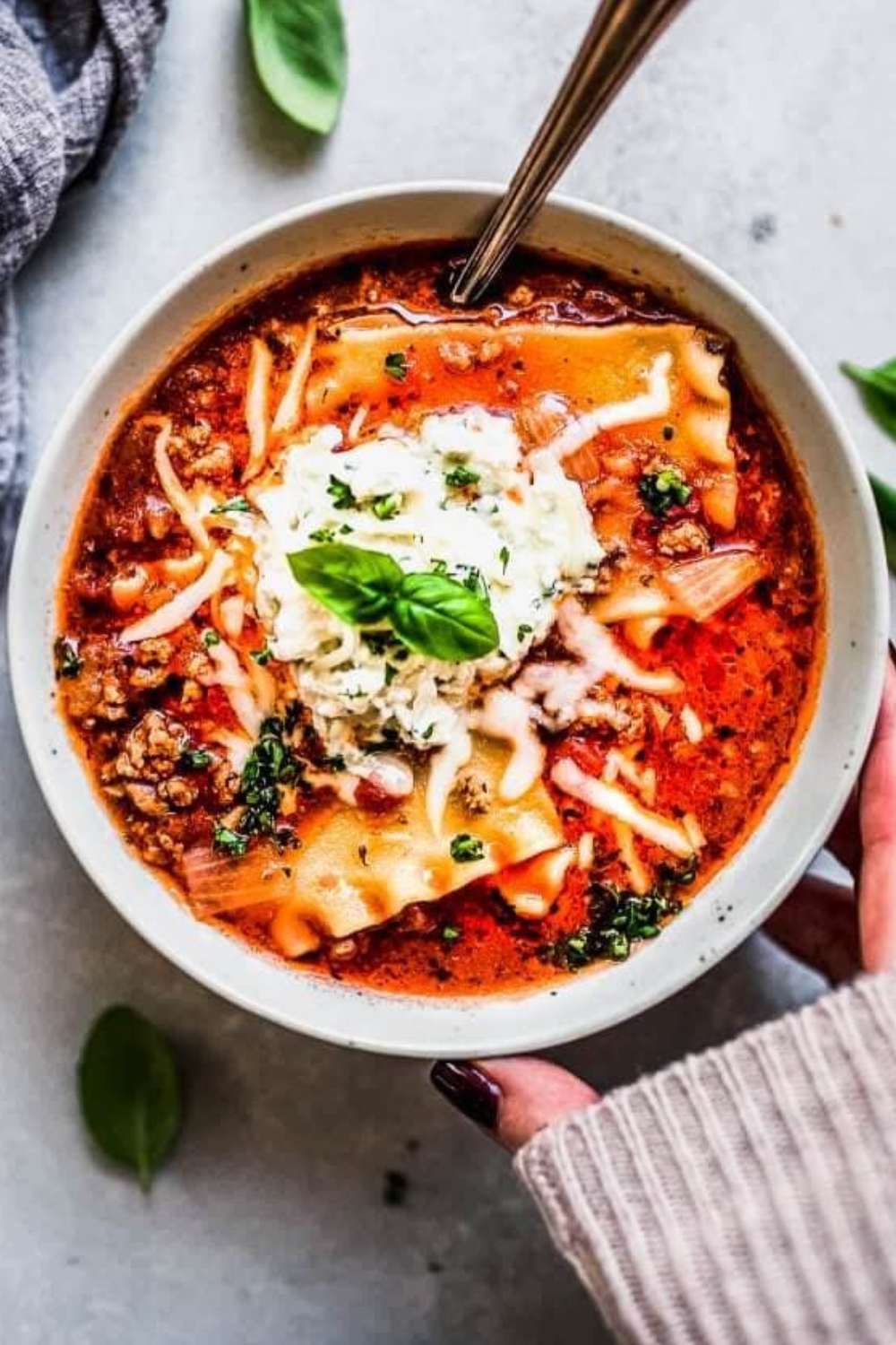 Hand holding bowl of instant pot lasagna soup.