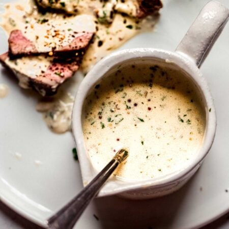 Mustard sauce for steak in small pouring vessel with spoon.