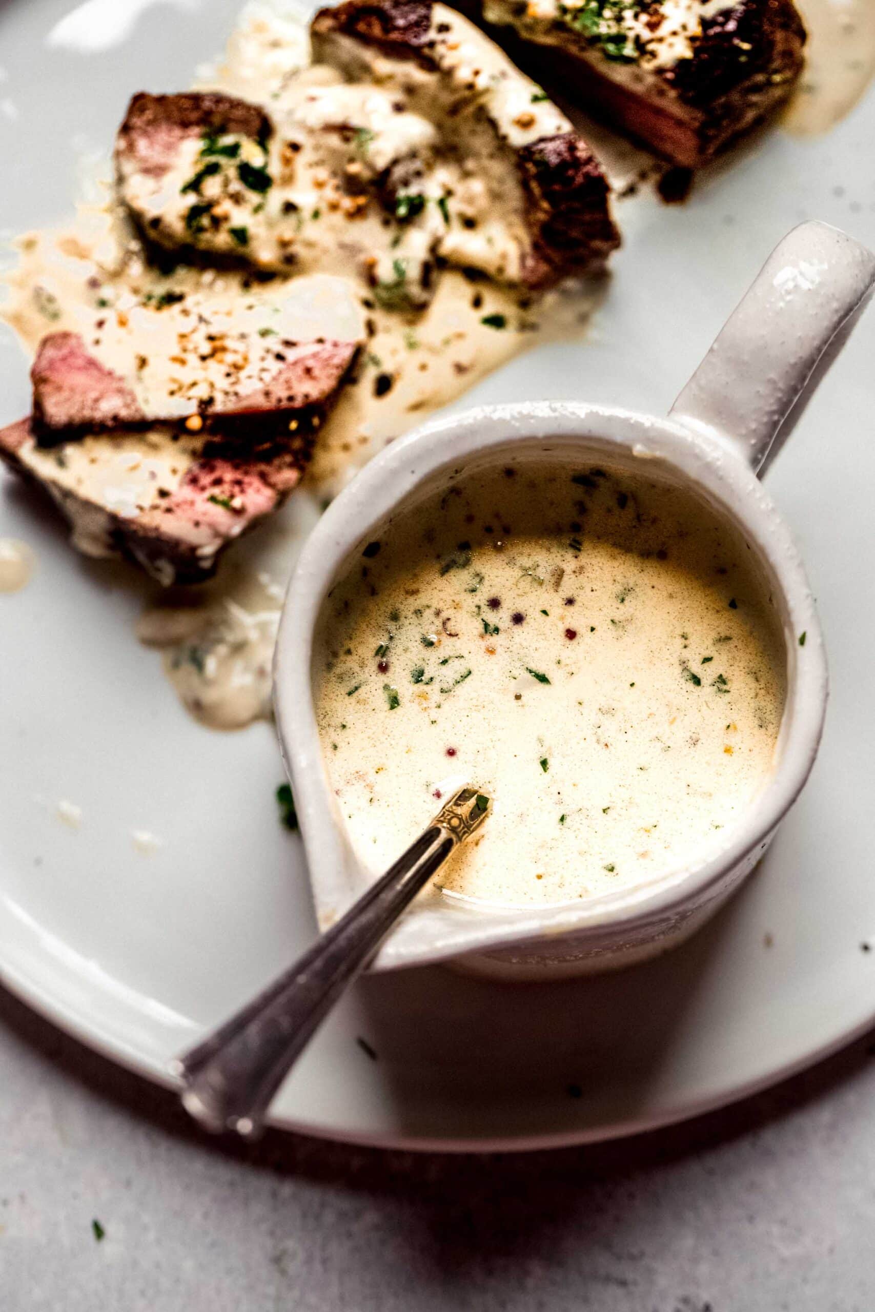 Mustard sauce for steak in small pouring vessel with spoon.