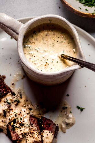 Mustard sauce for steak in small pouring vessel with spoon.