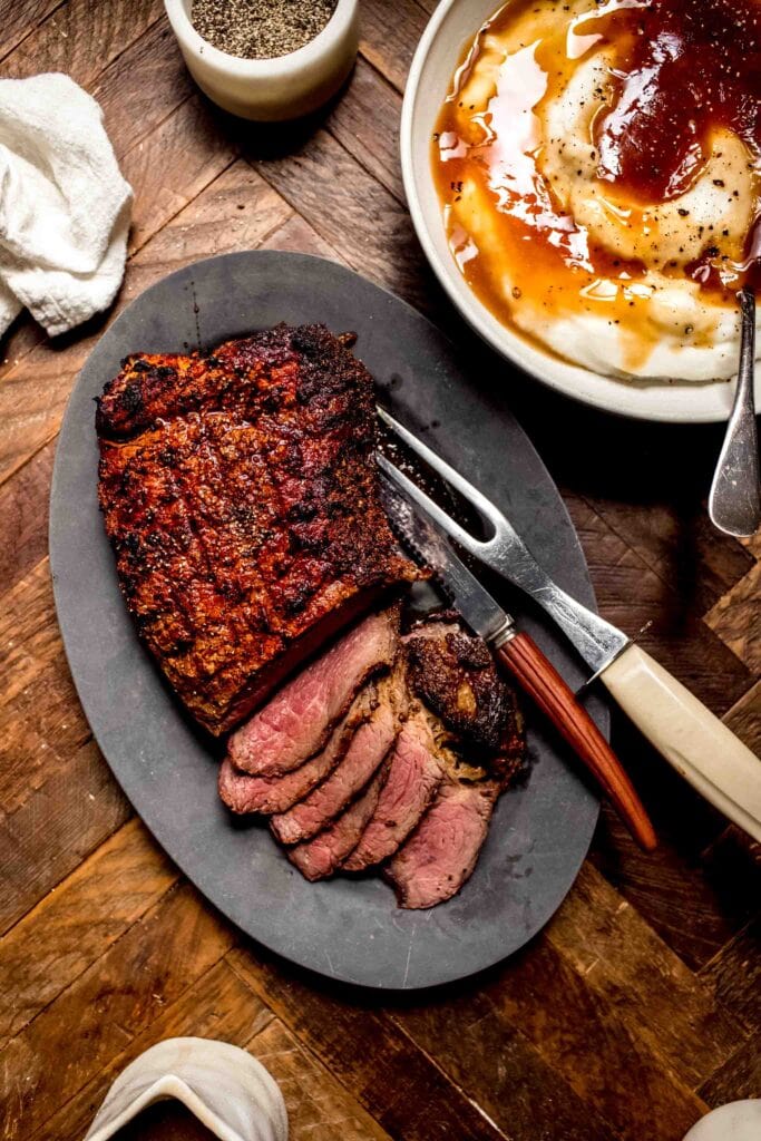 Sliced roast on serving platter next to bowl of mashed potatoes.