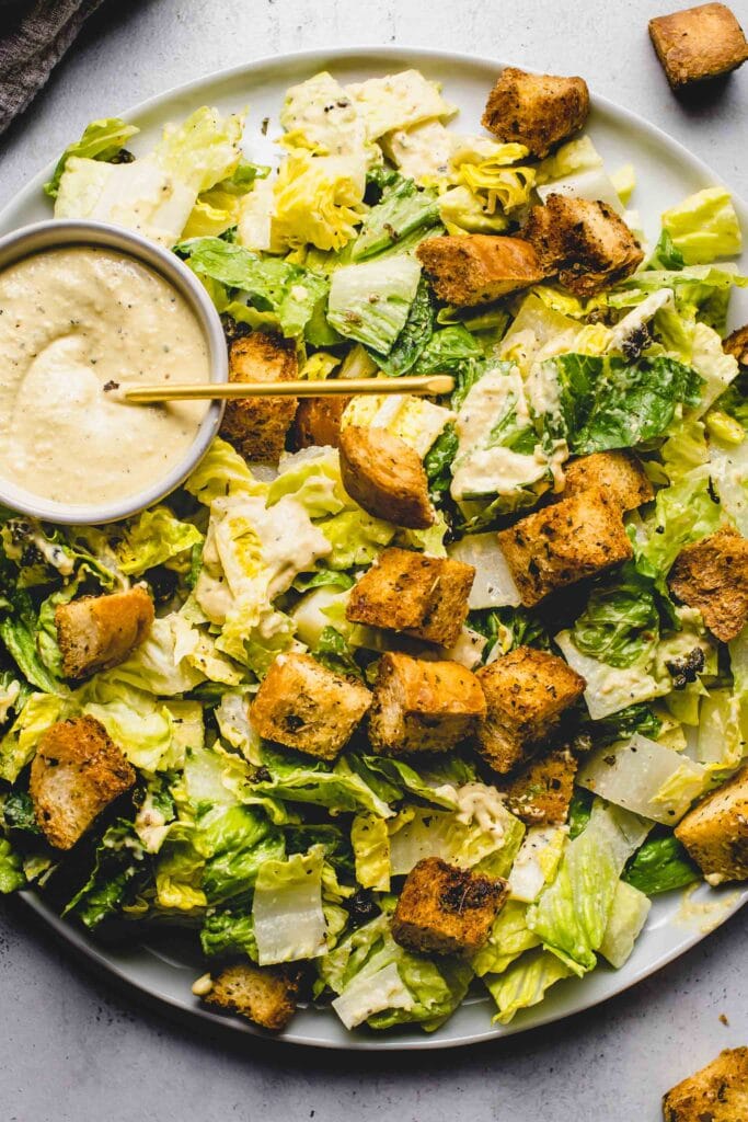 Salad topped with croutons next to small bowl of vegan caesar dressing.