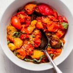 Air fried tomatoes in white bowl topped with basil sprigs.