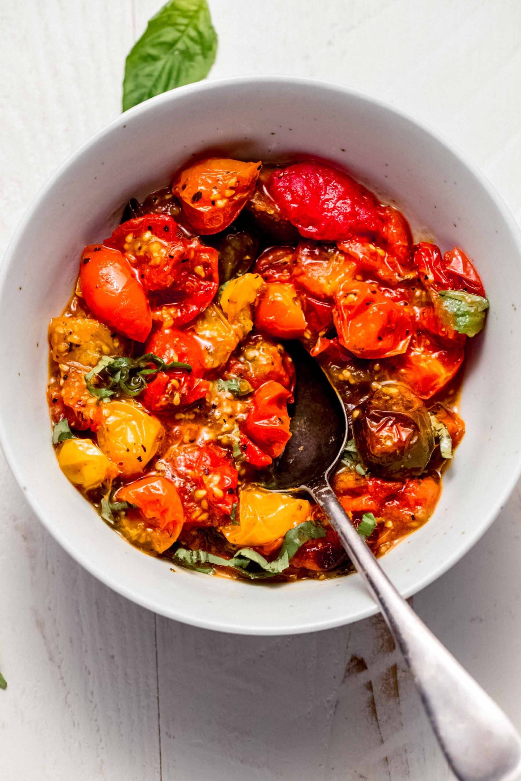 Air fried tomatoes in white bowl topped with basil sprigs.