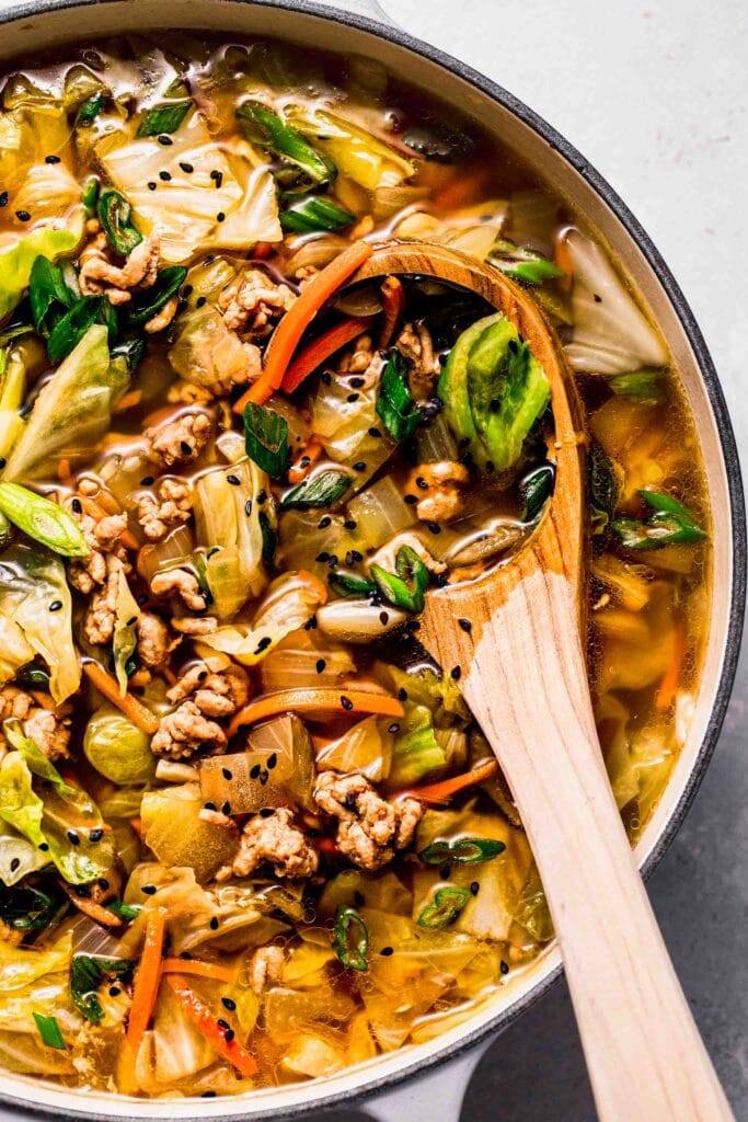 Close up of egg roll soup in pot with ladle.