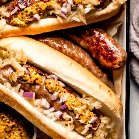 Bratwurst arranged on serving tray next to small bowls of mustard.