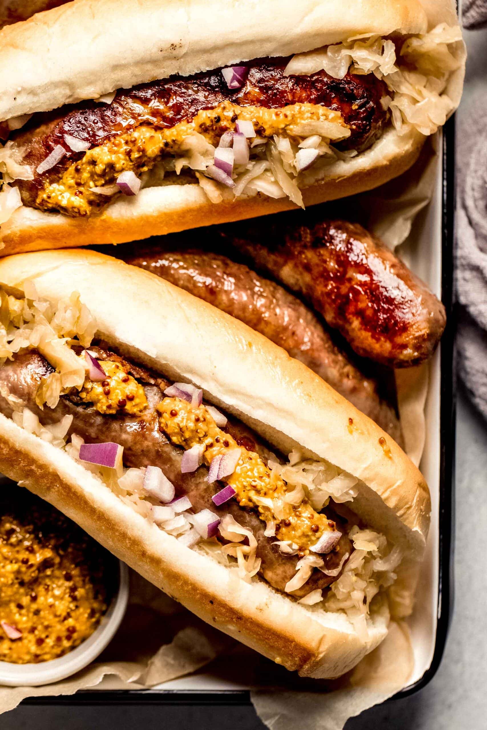 Bratwurst arranged on serving tray next to small bowls of mustard.