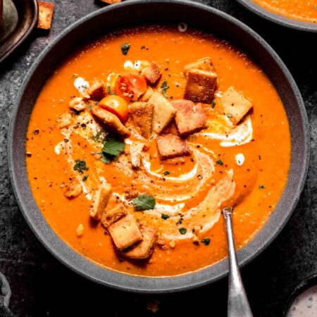 Indian tomato soup in grey bowl topped with naan croutons.