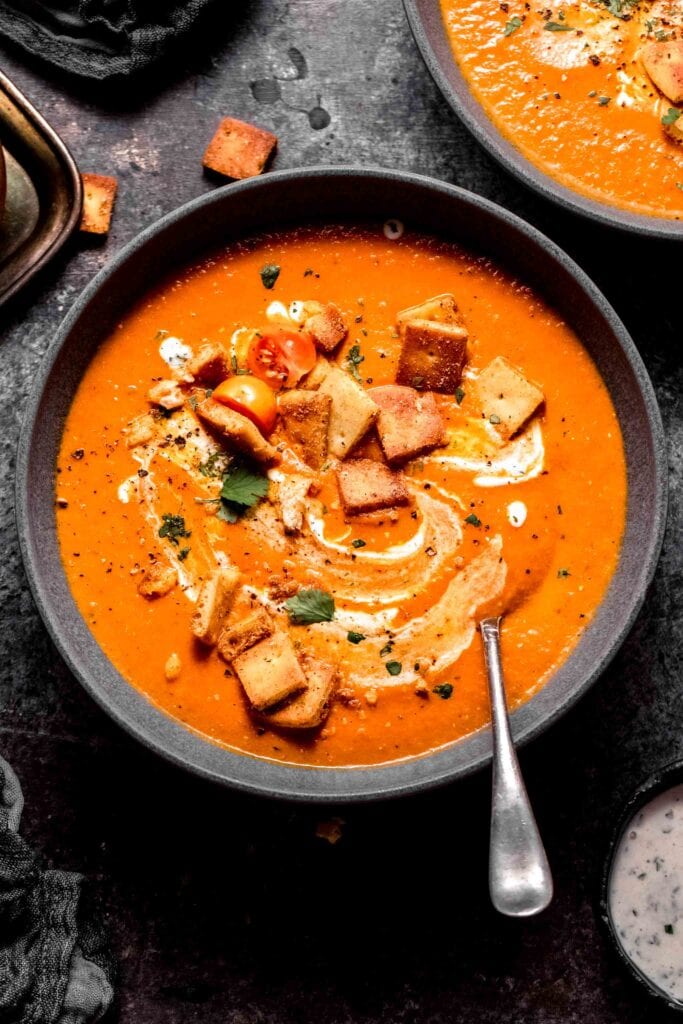 Indian tomato soup in grey bowl topped with naan croutons.