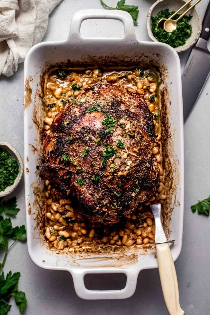 Roasted leg of lamb in baking dish with beans. 