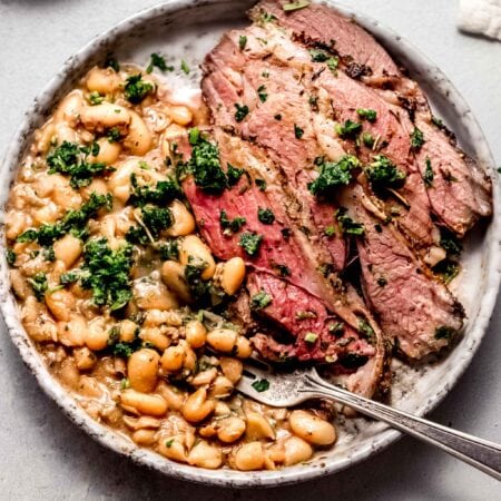 Sliced leg of lamb on plate with white beans and gremolata.