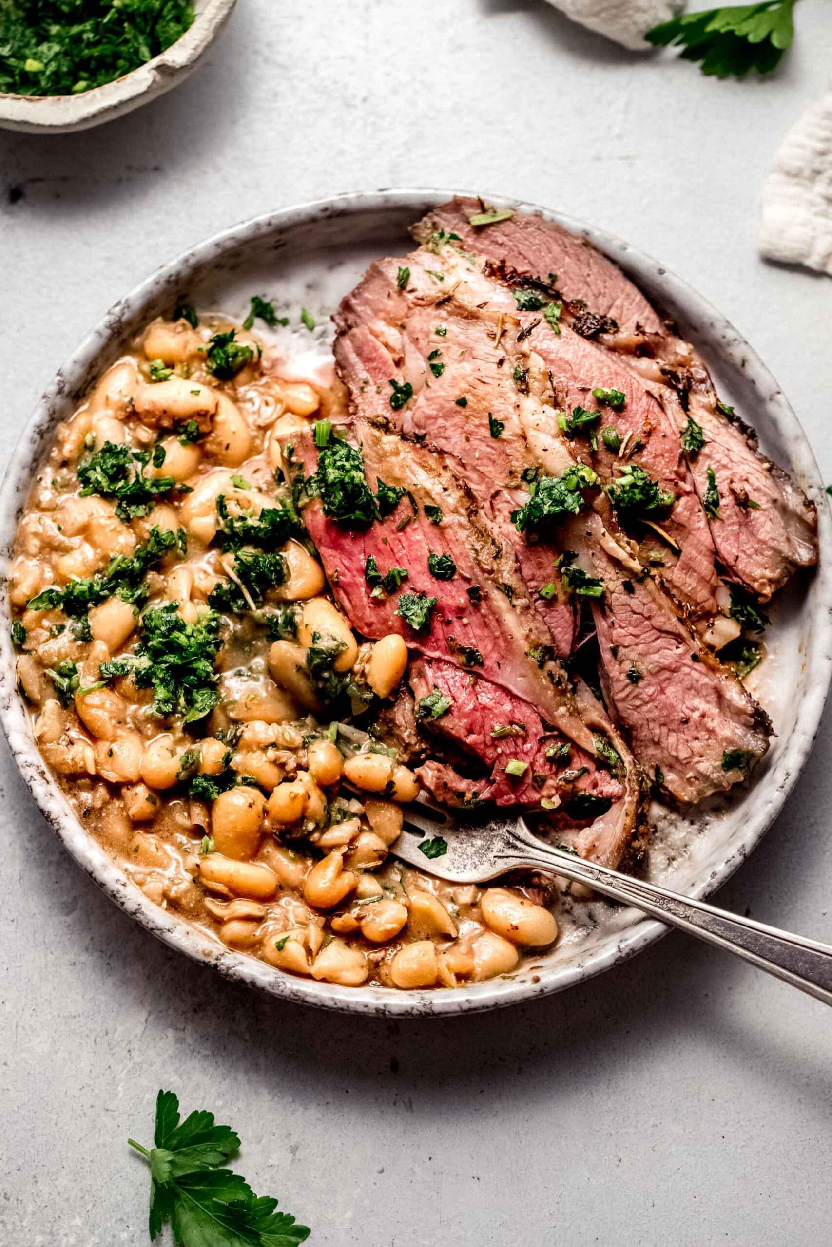 Sliced leg of lamb on plate with white beans and gremolata.