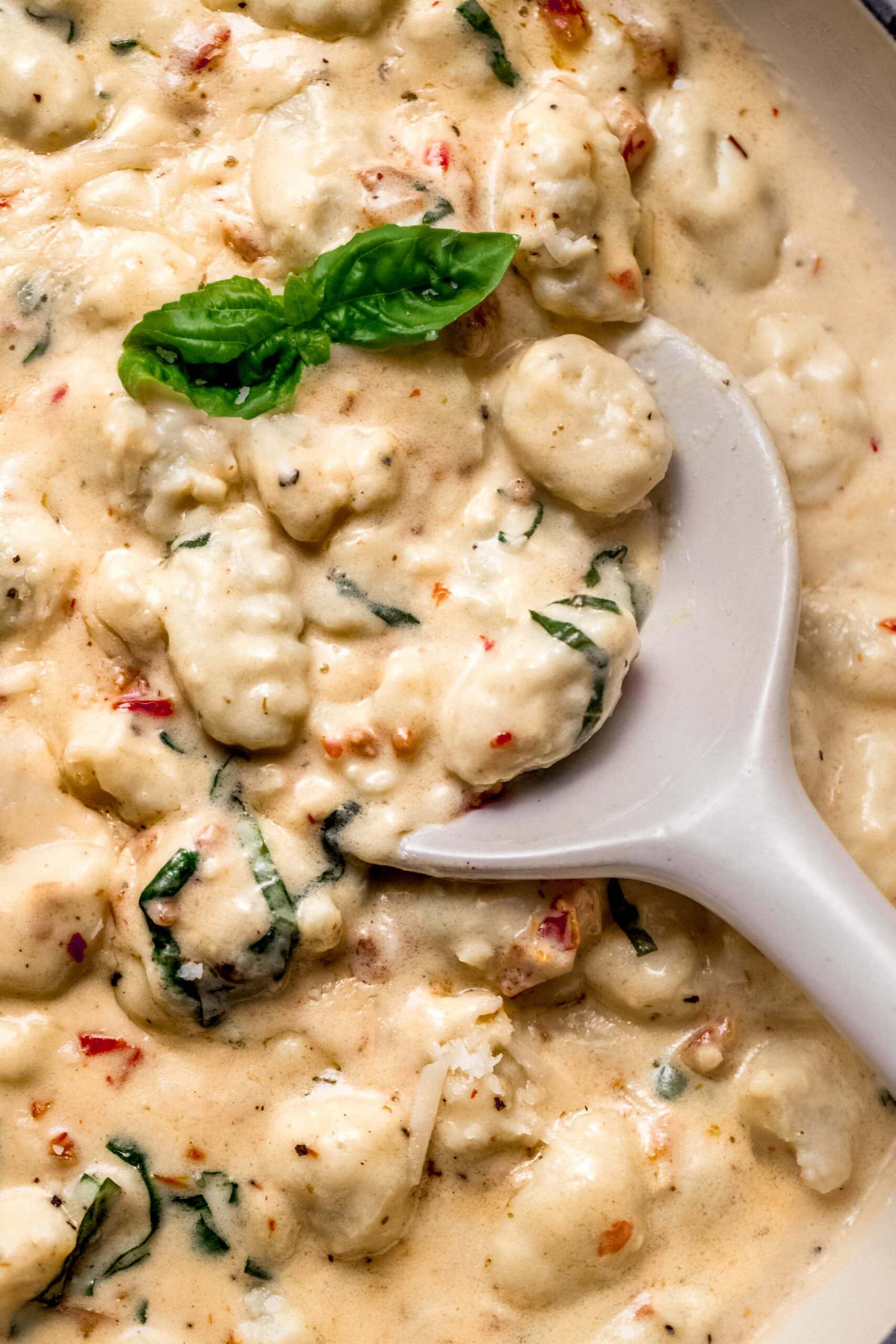 Prepared creamy gnocchi in skillet with serving spoon.