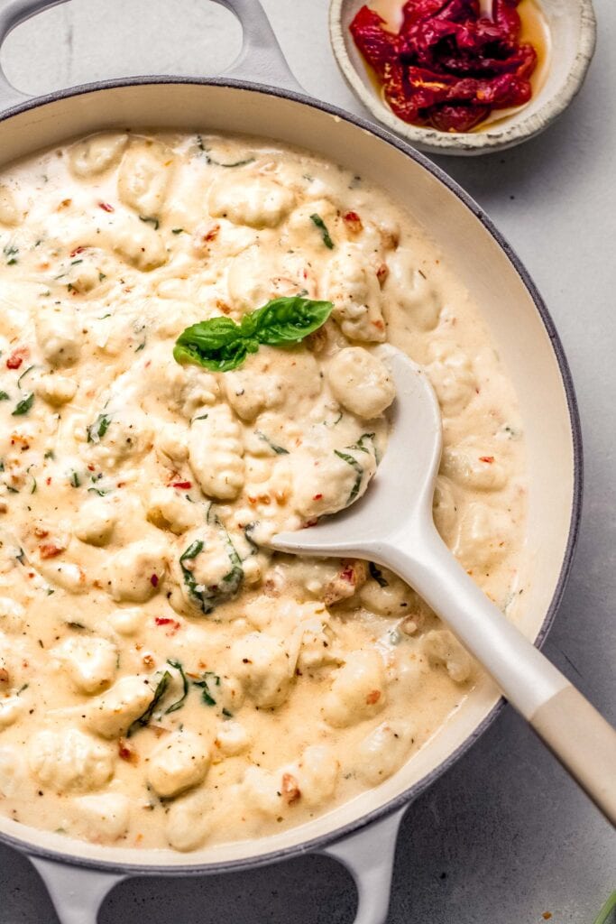 Gnocchi tossed with creamy sauce in skillet. 