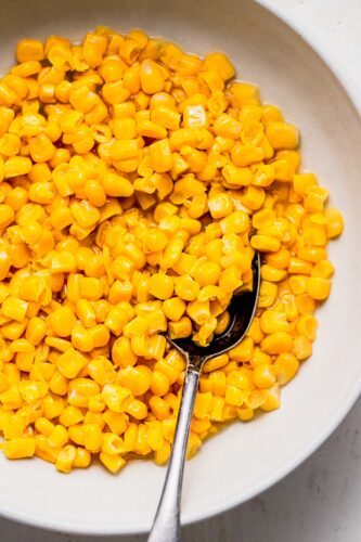 Overhead close up of cooked canned corn in serving bowl with spoon.