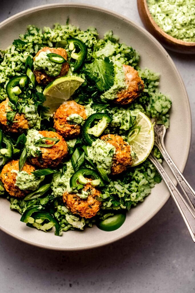 Close up of Prepared peruvian chicken meatballs served over green rice and drizzled with green sauce.