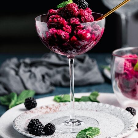 Side view of blackberry granita in champagne flute against black background.