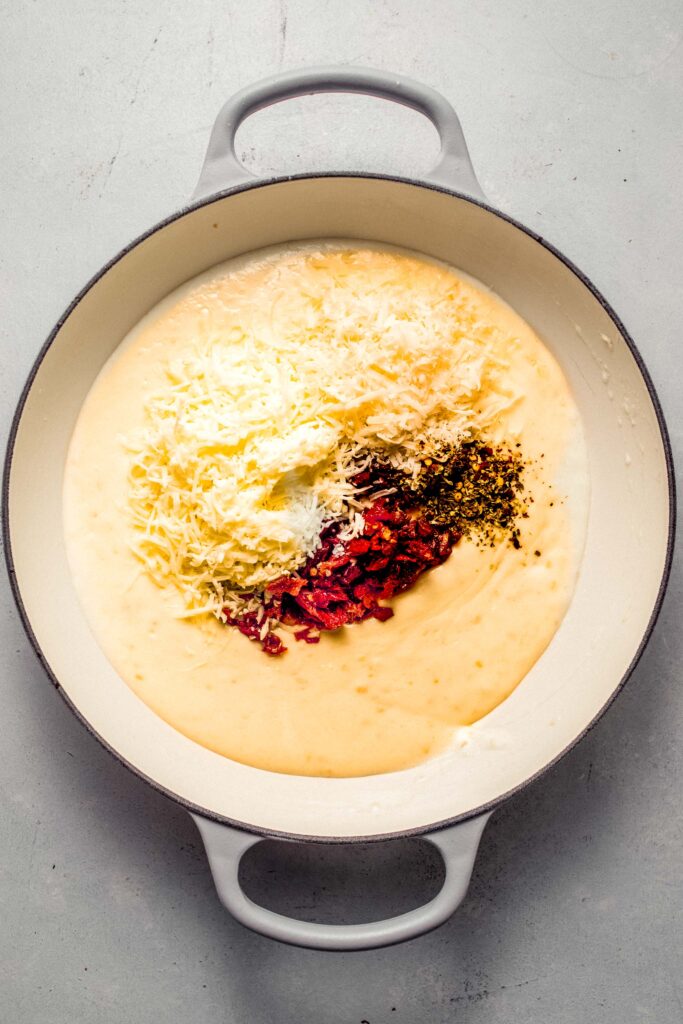Creamy sauce in skillet topped with cheese and sun dried tomatoes.