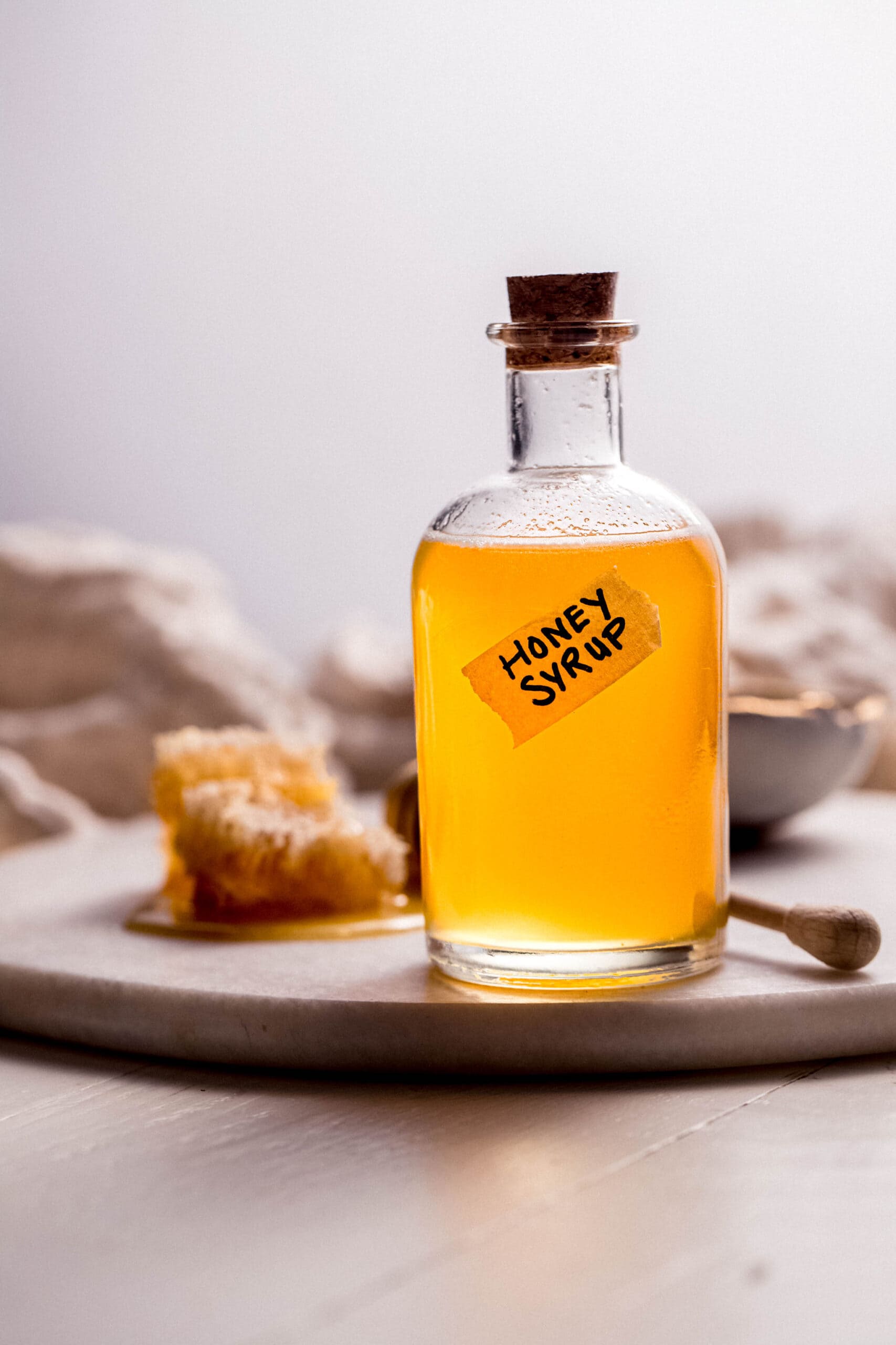 Side view of bottle of honey syrup with label next to honeycomb.