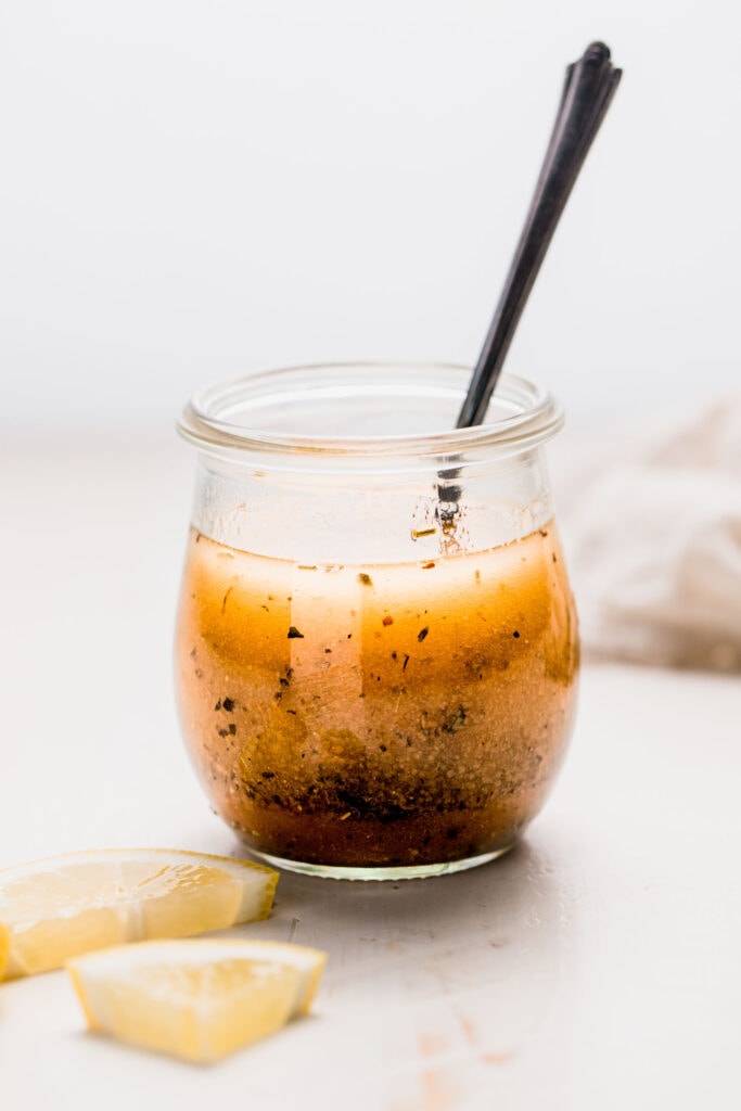 Side view of italian dressing in small jar with spoon.