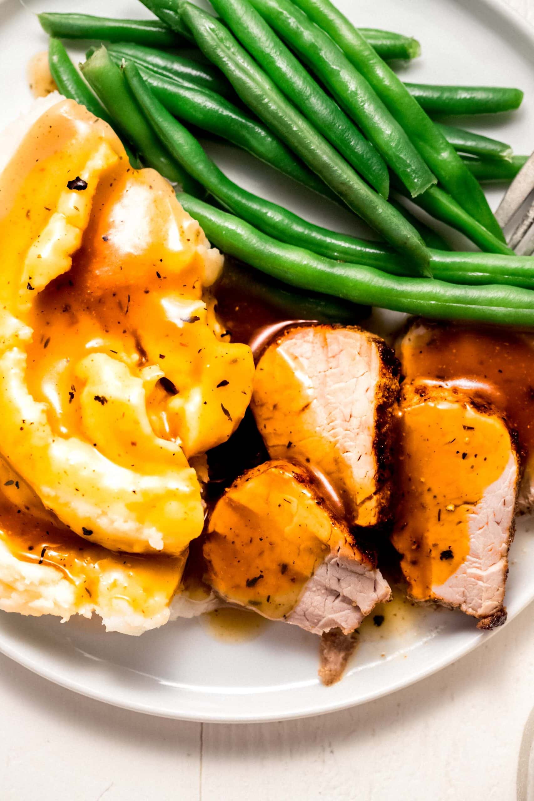 Pork medallions and mashed potatoes on plate drizzled with pork gravy.