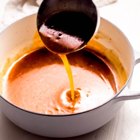 Ladle of pork gravy drizzling into saucepan.