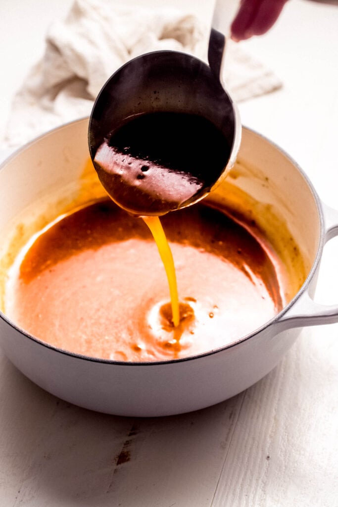 Ladle of pork gravy drizzling into saucepan.