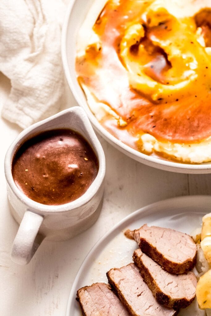 Gravy boat filled with pork gravy next to bowl of mashed potatoes.