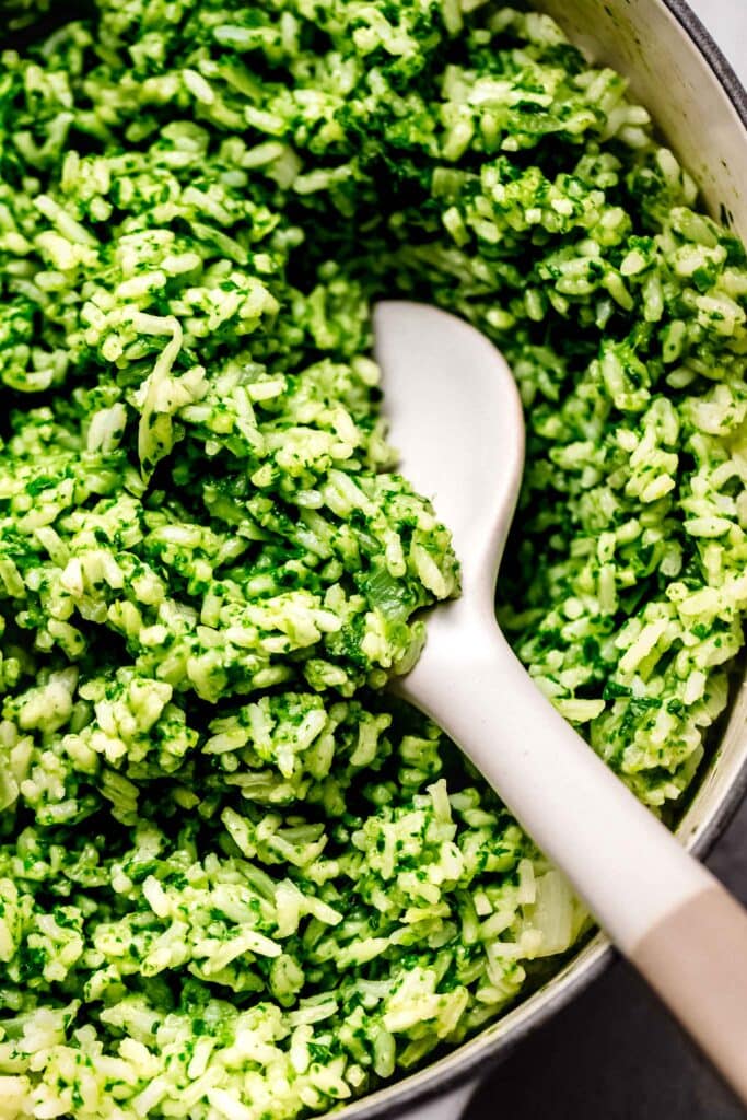 Overhead close up of spinach rice in skillet with serving spoon.
