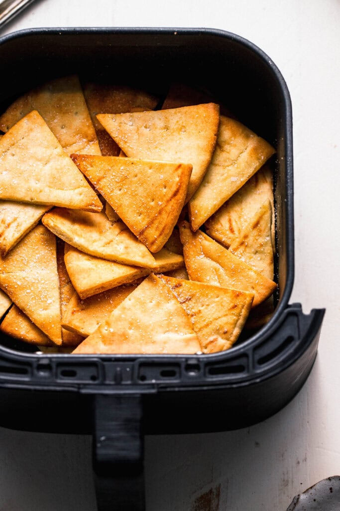 Cooked pita chips in air fryer basket.