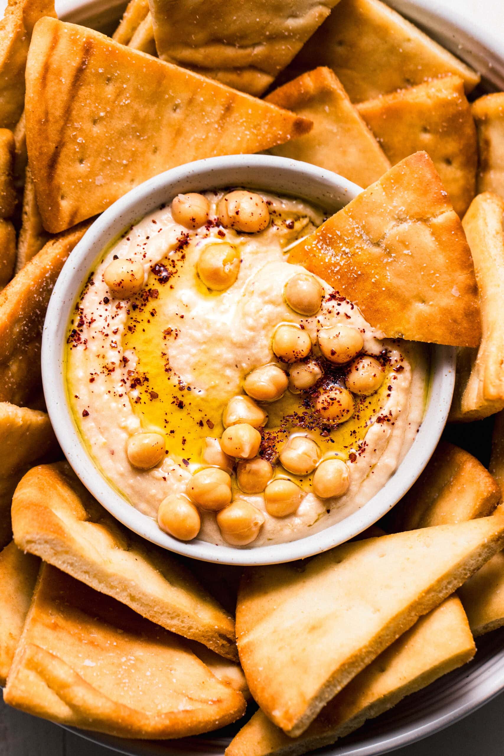 Air fryer pita chips arranged in bowl with small bowl of hummus.