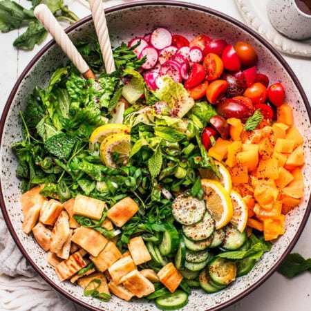 Fattoush salad assembled in large bowl with serving tongs.
