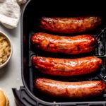 Air fryer cooked sausage links next to small bowl of mustard.