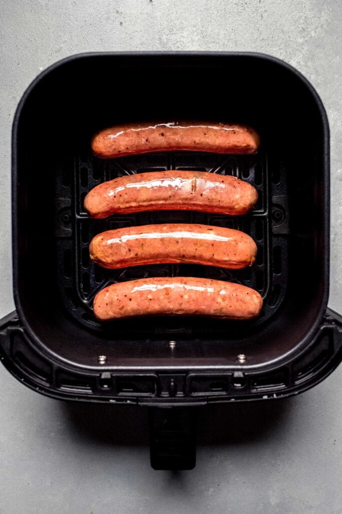 Uncooked sausages in air fryer basket.