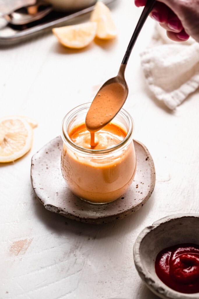 Spoon drizzling sriracha mayo into small glass jar.