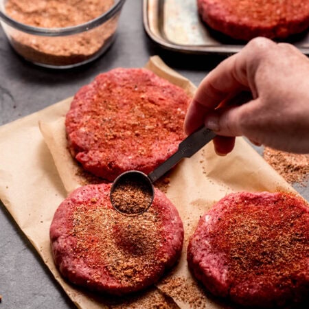 Hand sprinkling seasoning onto burger patties.