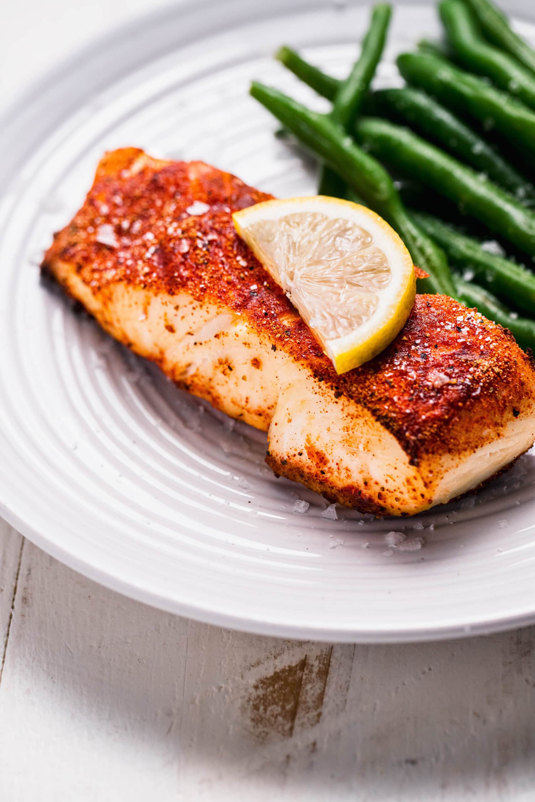 Side view of prepared seasoned halibut filet air fried and served on plate next to green beans.