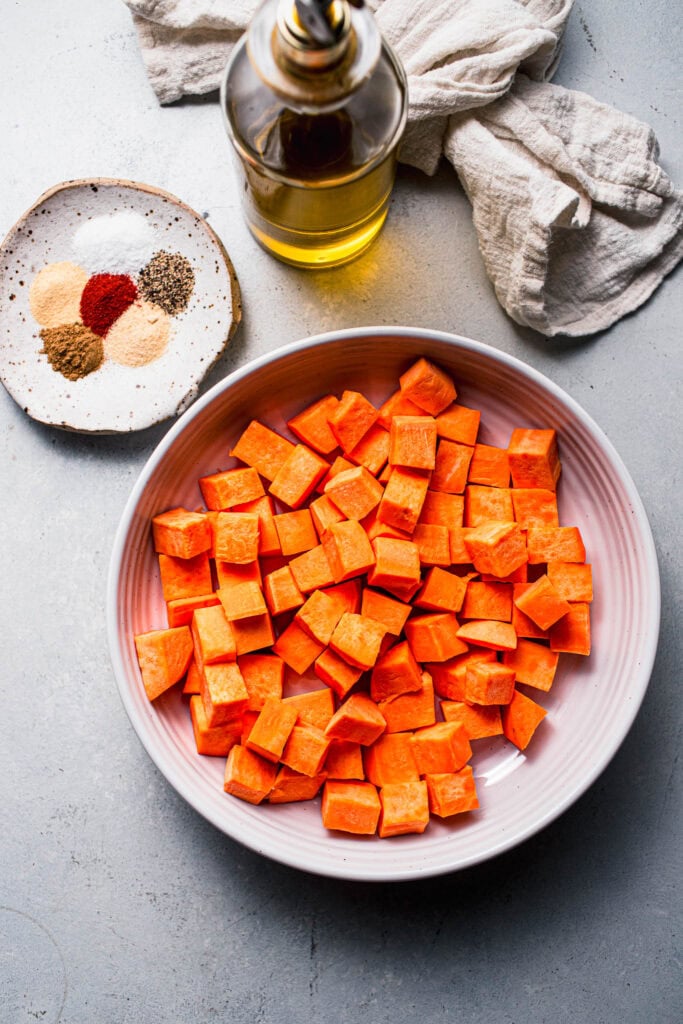 Sweet potato cubes in bowl next to seasonings.