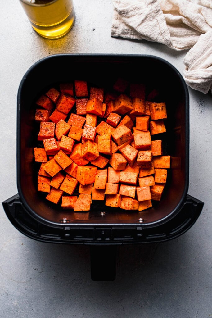 Uncooked sweet potato cubes in air fryer basket.
