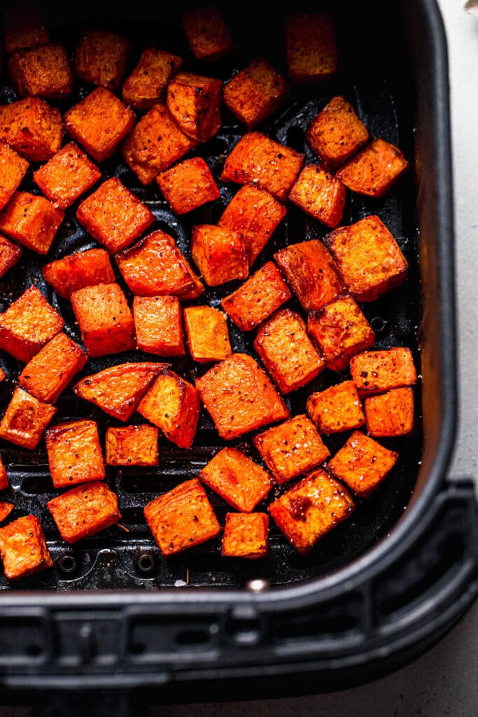 Golden sweet potatoes in air fryer basket.